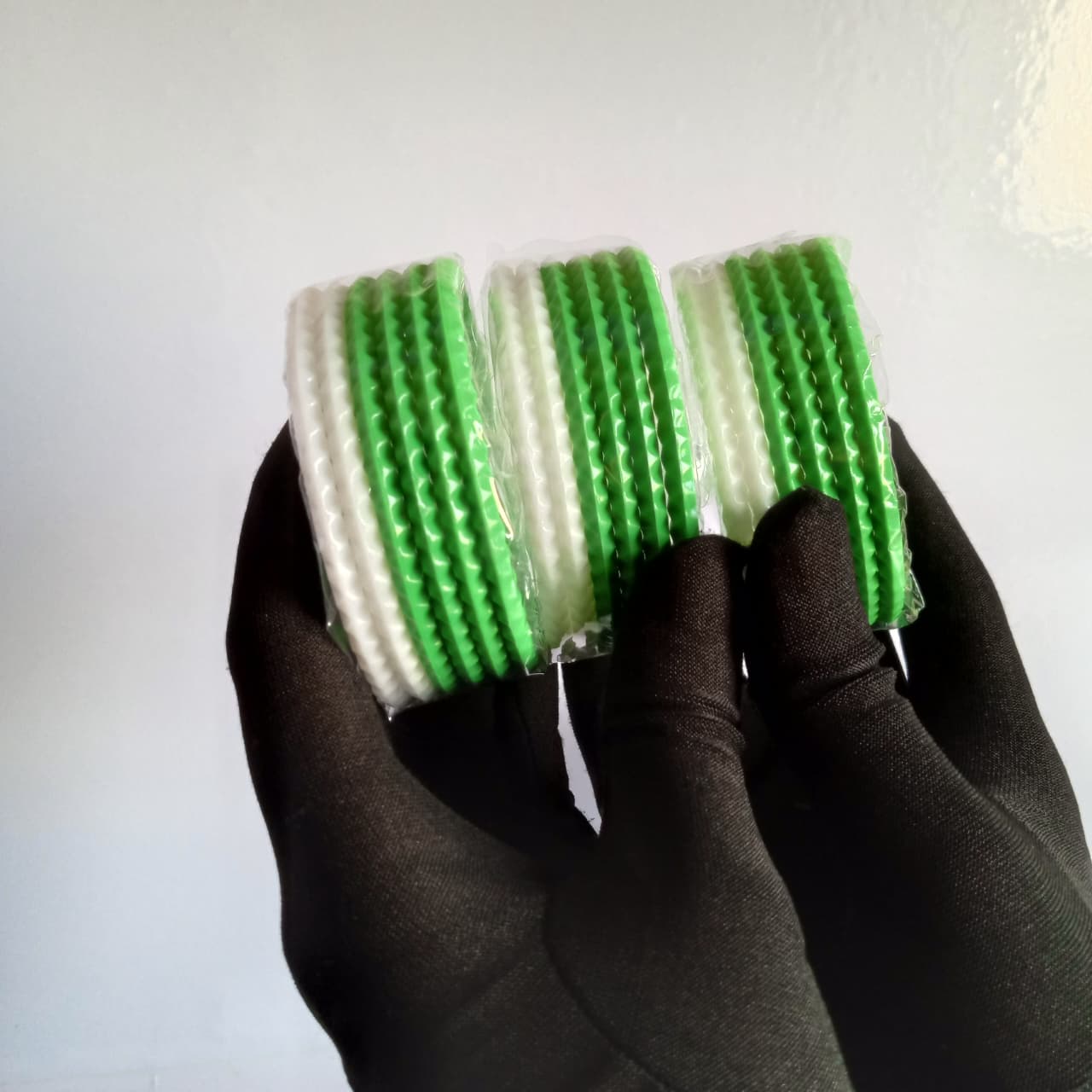 Three rolls of textured green and white hair ties held in a hand wearing a black glove against a plain light background.